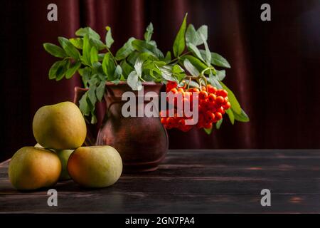 Rowan branch with berries and green apples on dark wooden background and textile with copy space Stock Photo