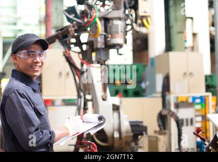 Industrial engineer standing in front of the robot and holding a notebook Stock Photo