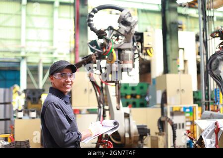 Industrial engineer standing in front of the robot mechine writing in notebook Stock Photo