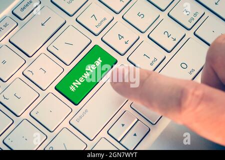 Close up of finger on keyboard button with NEW YEAR word. A male finger presses a color button on a gray silver keyboard of a modern laptop. Button wi Stock Photo