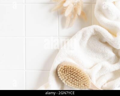 Bath background flat lay with white towels, wood brush and dry flowers on white tiles background. Top view. Copy space Stock Photo