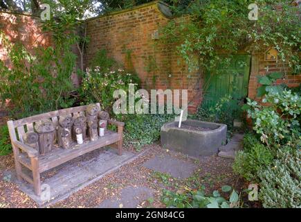 A corner of the walled garden in Sheffield's Meersbrook Park with a wooden bench, stone trough and carved figures. Stock Photo