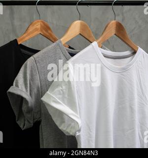 Young male in front blank black t-shirt Roll up sleeves template, Three color black white gray hang on cement background for your design concept Stock Photo