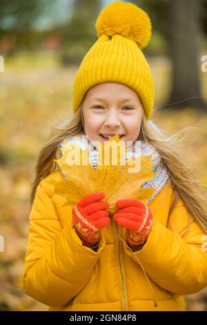 Little blond girl in yellow clothing with yellow leaf, autumn Stock Photo