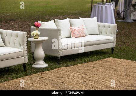 An outdoor party or wedding set up with furniture including a couch, table and floral bouquets Stock Photo