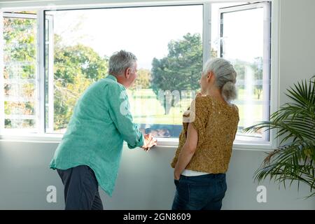 Back view of caucasian senior couple standing at window and talking Stock Photo