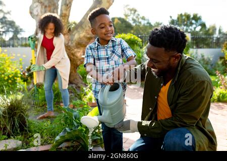 Happy african american father and son watering plants together Stock Photo