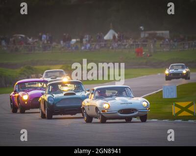 E Type Jaguar, AC Cobra and Aston Martin racing at sunset at the Goodwood Revival 2021, West Sussex, uk Stock Photo
