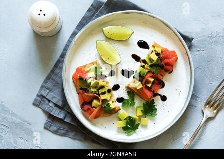 Avocado and salmon sandwiches with balsamic sauce and cilantro on old olive board. Top view Stock Photo