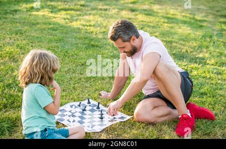 happy family of father man and son child playing chess on green grass in park outdoor, strategy Stock Photo