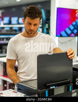 Young bearded male client in casual clothes checking quality of printer while choosing device in spacious electronics shop Stock Photo