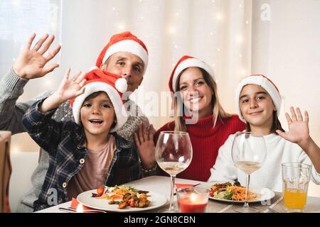 Portrait of happy family looking at camera during vegan Christmas dinner party wearing Santa Claus hats - Focus on little son Stock Photo
