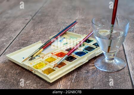 Selective focus.of an artists  set of half pan watercolor paints in a plastic folding box with palette and paintbrushes for watercoloring Stock Photo