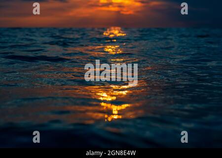Cloudy sunset with warm colors and surface of ocean with reflection. Stock Photo
