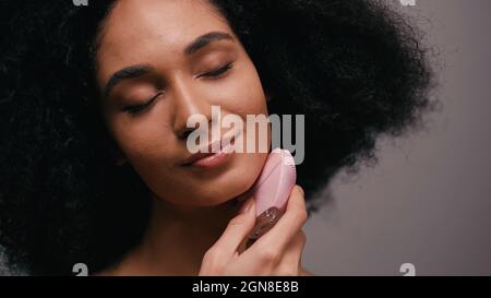 pleased african american woman using silicone cleanser on face isolated on grey Stock Photo