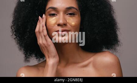 close up of african american woman applying hydrogel eye patches isolated on grey Stock Photo