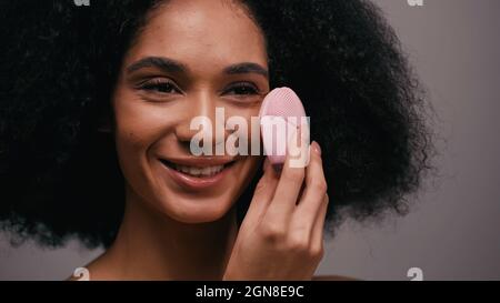 happy african american woman using silicone cleansing device on face isolated on grey Stock Photo