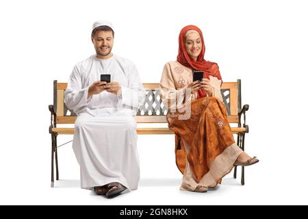 Young man and woman in ethnic clothes sitting on a bench and using smartphones isolated on white background Stock Photo