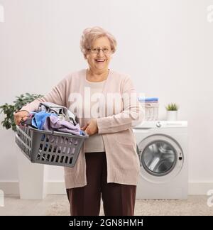 Elderly woman holding a laundry basket with clothes inside a bathroom Stock Photo