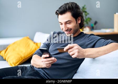 Man using smart phone while making payment through credit card at home Stock Photo