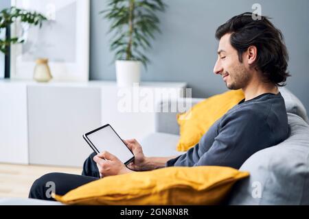 Man using digital tablet while sitting on sofa Stock Photo