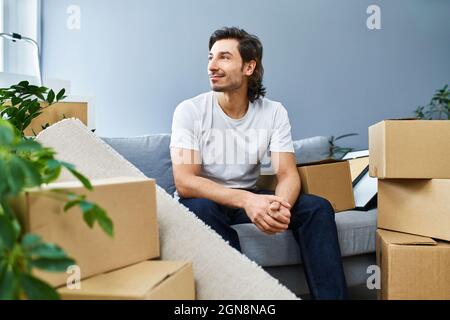 Man sitting amidst cardboard boxes on floor in living room of new house  stock photo
