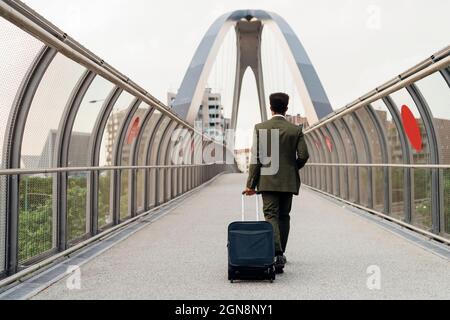 Businessman walking with wheeled luggage on bridge Stock Photo