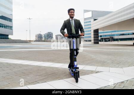 Young businessman riding electric push scooter in city Stock Photo