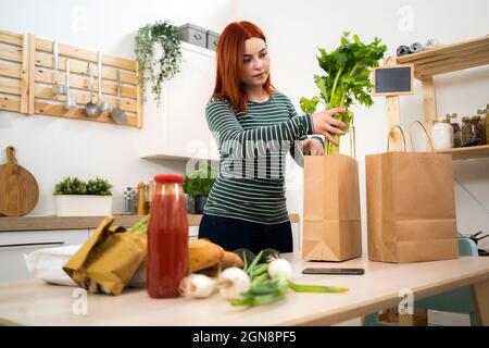 Woman removing vegetables from paper bags on table Stock Photo
