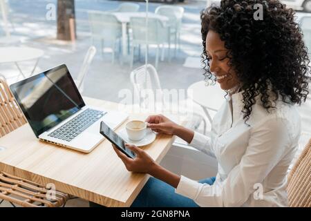 Female freelancer using mobile phone while sitting at cafe Stock Photo