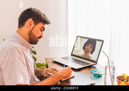 Male doctor taking notes while listening to female patient on video call through laptop Stock Photo