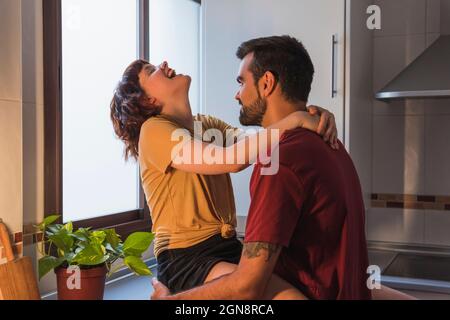 Bearded man looking at girlfriend laughing in kitchen Stock Photo