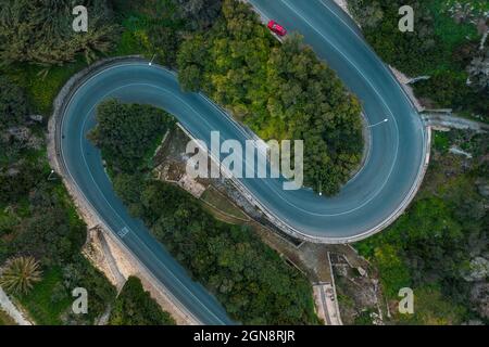 Aerial view of a winding asphalt road cutting through lush green ...