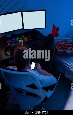 Boy using smart phone while sitting on chair by computer table Stock Photo