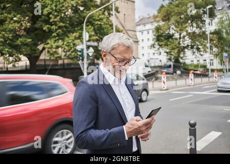 Smiling male professional using smart phone on road Stock Photo