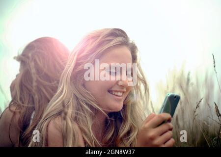 Happy girl using smart phone with friend in background during vacation Stock Photo