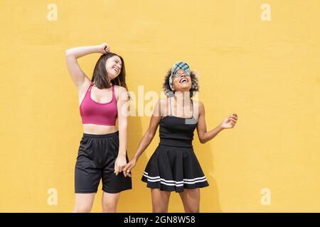Cheerful multi-ethnic friends dancing in front of yellow wall Stock Photo