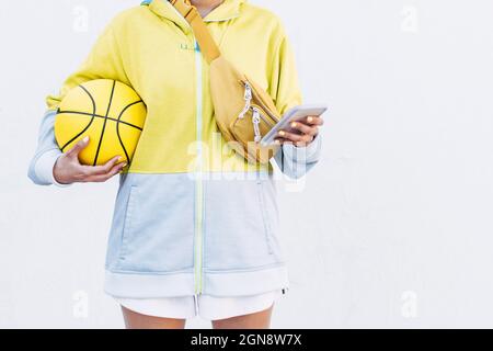 Young woman with basketball using smart phone in front of white wall Stock Photo
