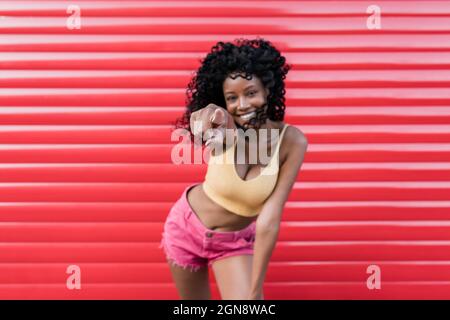 Smiling young woman pointing while standing in front of red shutter Stock Photo