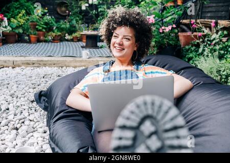 Smiling woman with laptop relaxing on bean bag Stock Photo