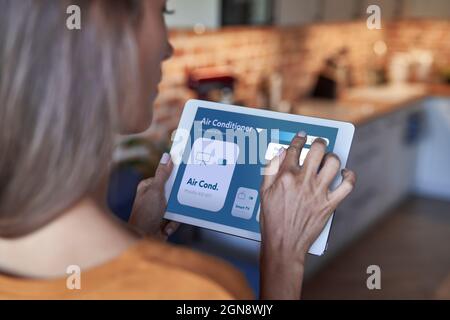 Woman adjusting air conditioner through digital tablet at home Stock Photo