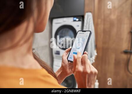 Woman operating washing machine through mobile application at home Stock Photo