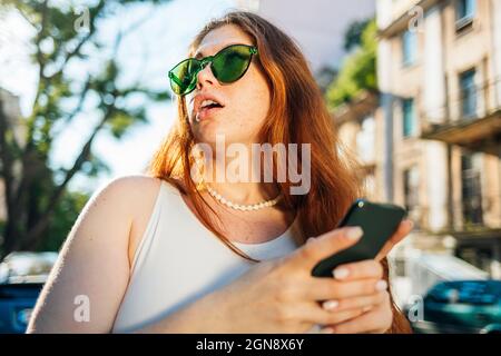 Surprised young woman in green sunglasses holding mobile phone Stock Photo