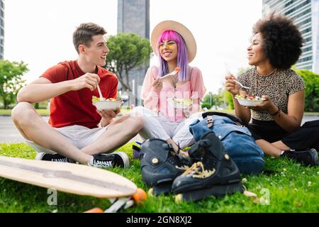 Happy young friends eating salad while sitting at park Stock Photo