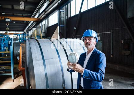 Male engineer with hardhat holding globe while standing in steel mill Stock Photo