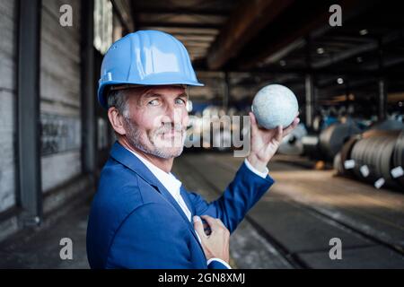 Male engineer with hardhat holding globe at warehouse Stock Photo