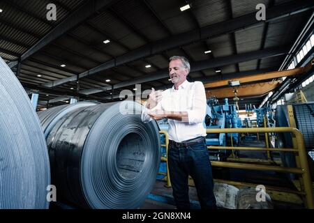Senior businessman rolling sleeves while standing in steel mill Stock Photo