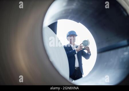 Businessman wearing hardhat holding globe seen through rolled sheet metal Stock Photo