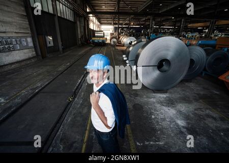 Thoughtful male engineer with hardhat and blazer standing in warehouse Stock Photo