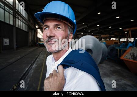 Male engineer with hardhat holding blazer while looking away Stock Photo